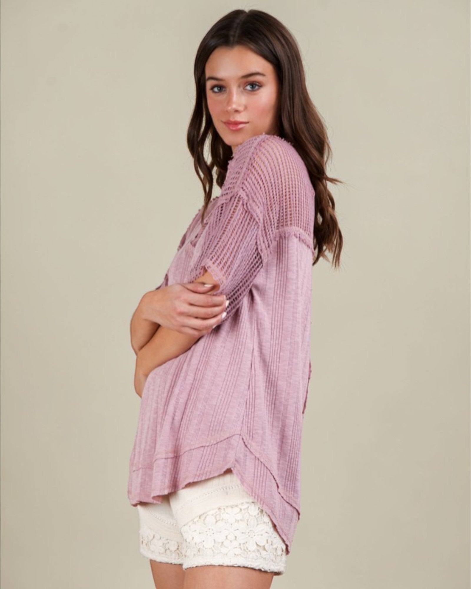 Woman wearing a pink textured top and white shorts on a beige background