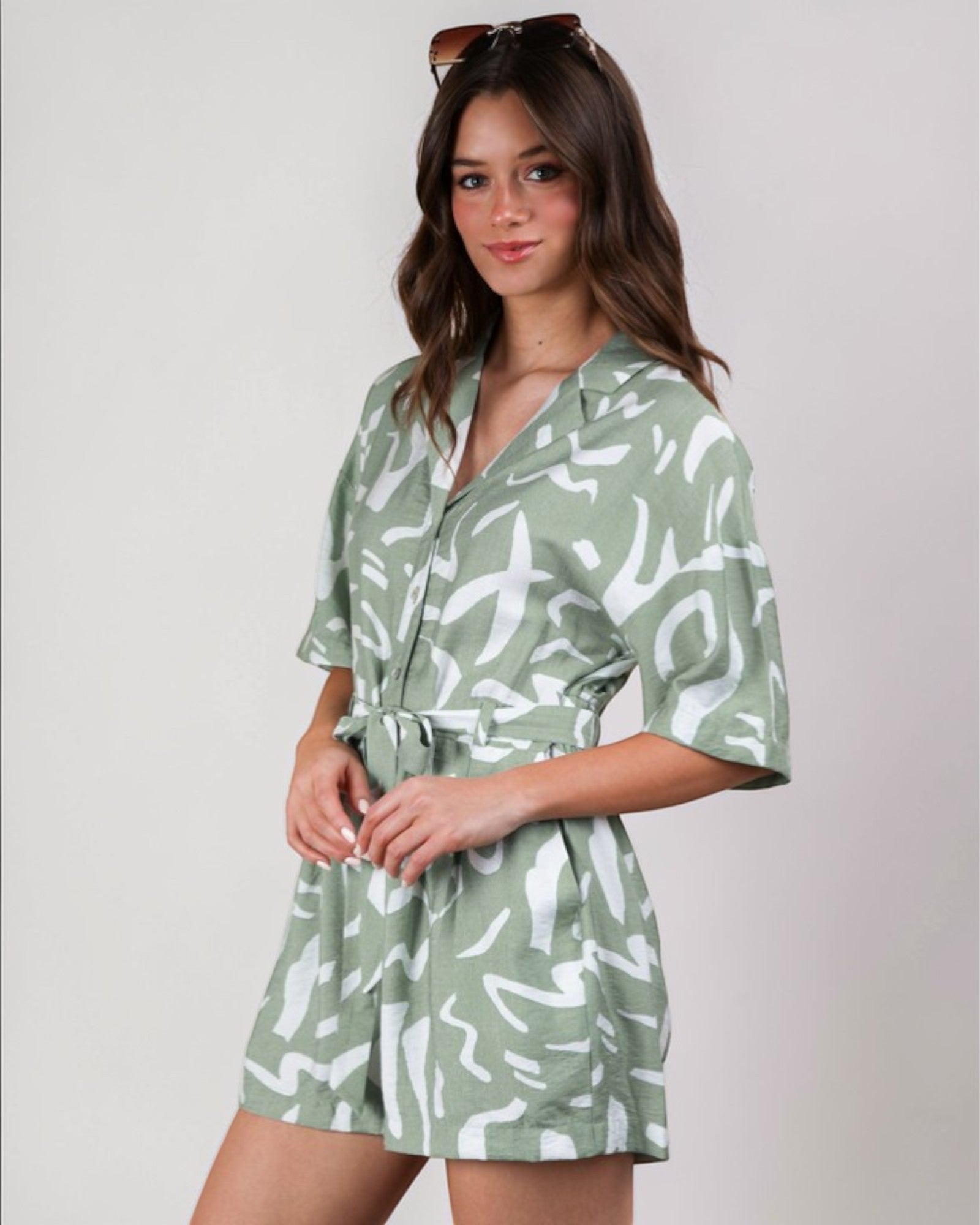 Woman wearing a green and white patterned romper against a plain background