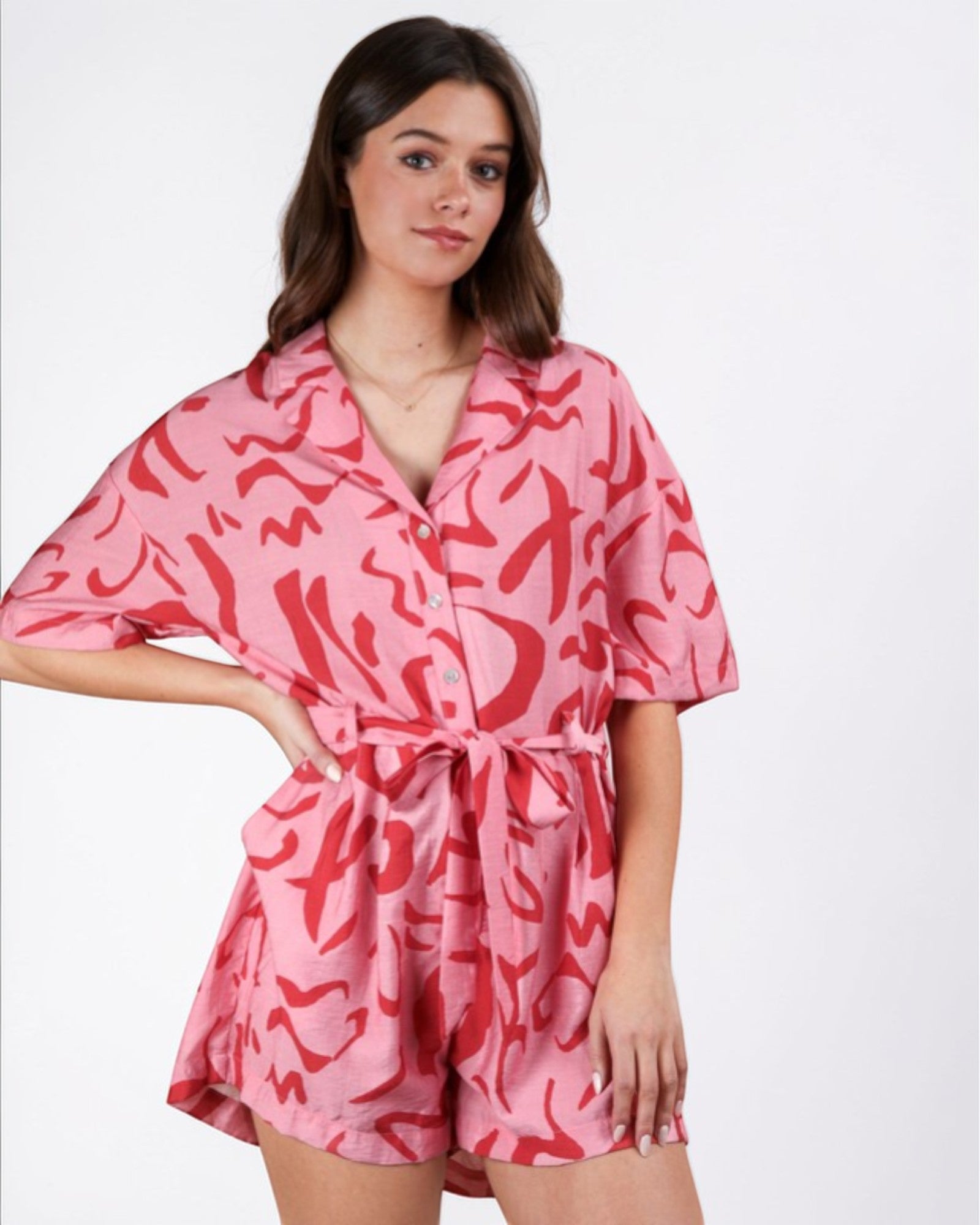 Woman wearing a pink romper with red abstract pattern on a white background