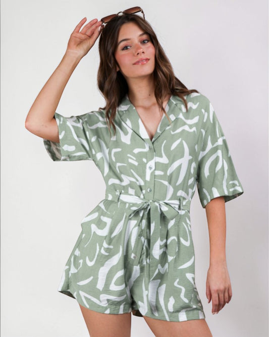 Woman wearing a green and white patterned romper against a plain background