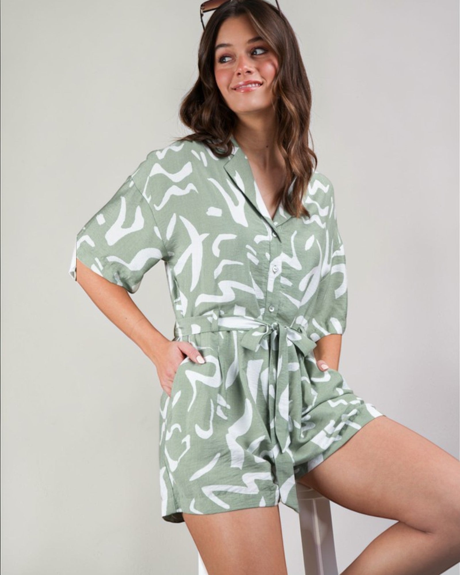 Woman wearing a green and white patterned romper against a plain background