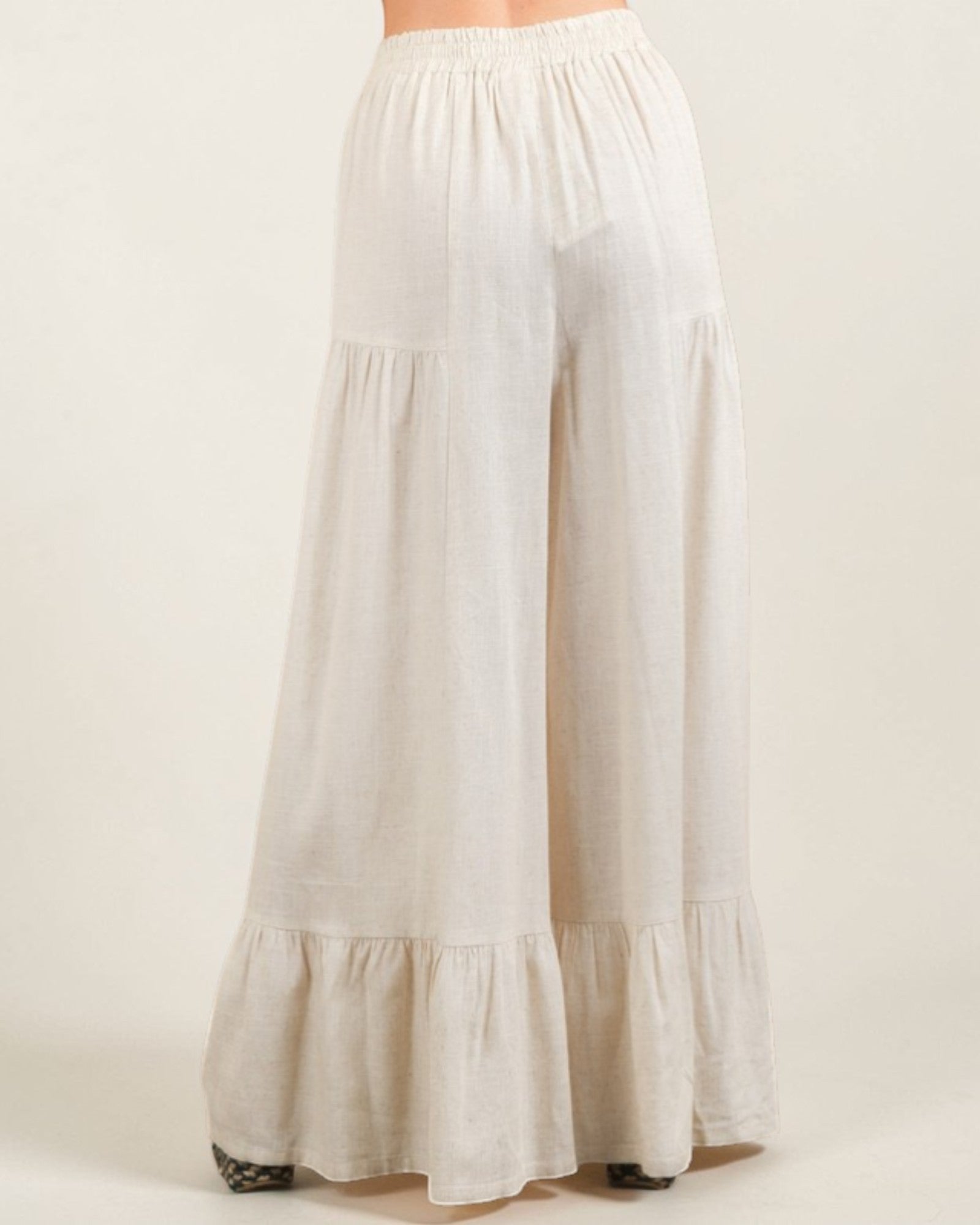 Beige wide-leg pants with ruffled bottom on a white background