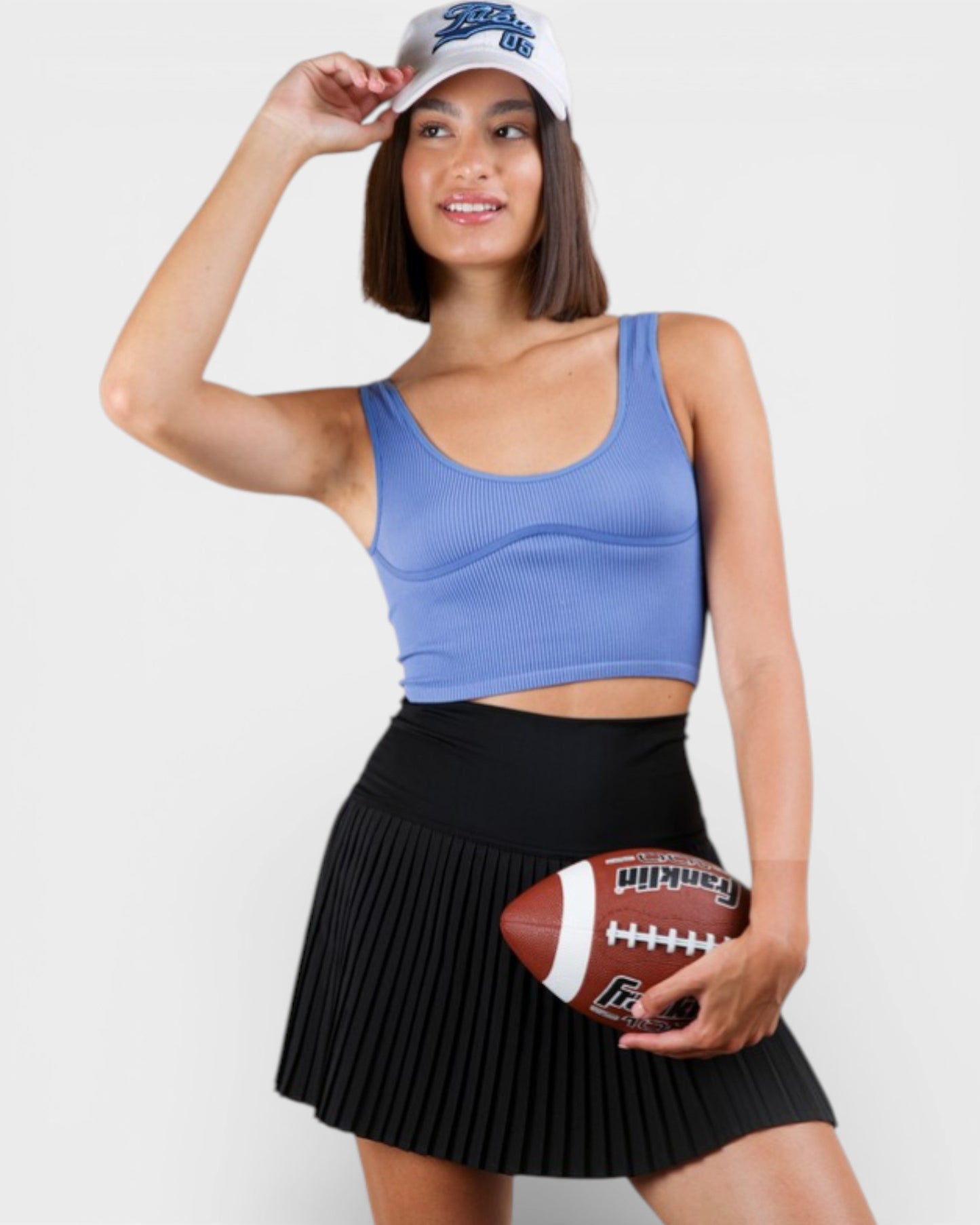 Woman wearing a blue sports bra and black skirt, holding a football against a white background