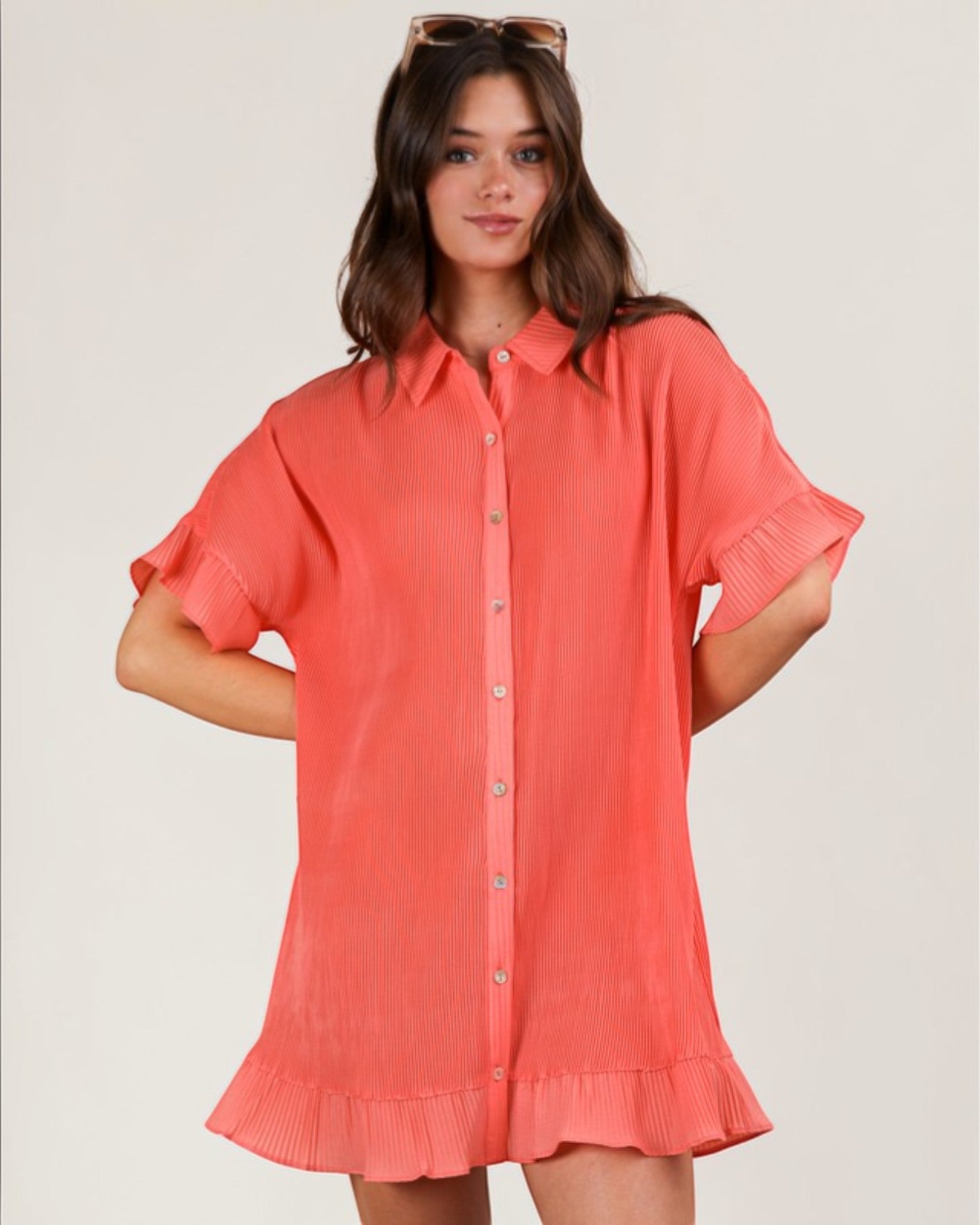 Woman wearing a coral dress with short sleeves on a plain background