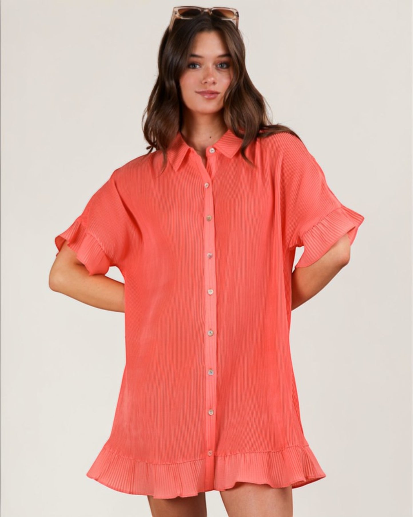 Woman wearing a coral dress with short sleeves on a plain background