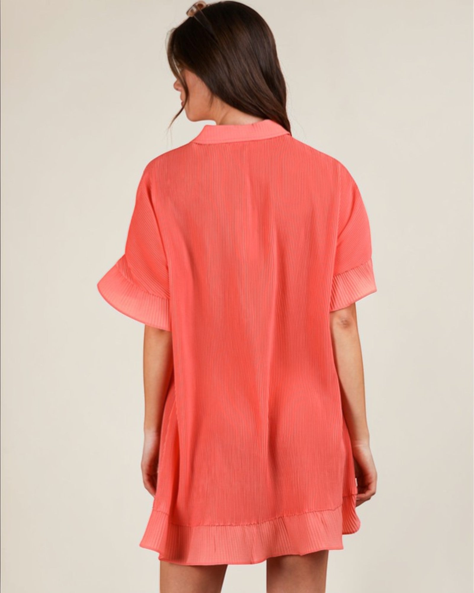 Woman wearing a coral dress against a plain background