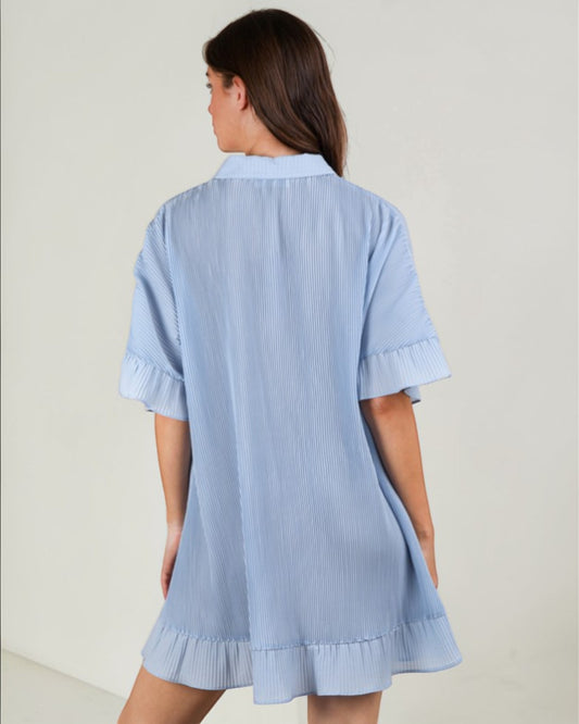 Woman wearing a light blue dress with ruffled sleeves and hem on a plain background