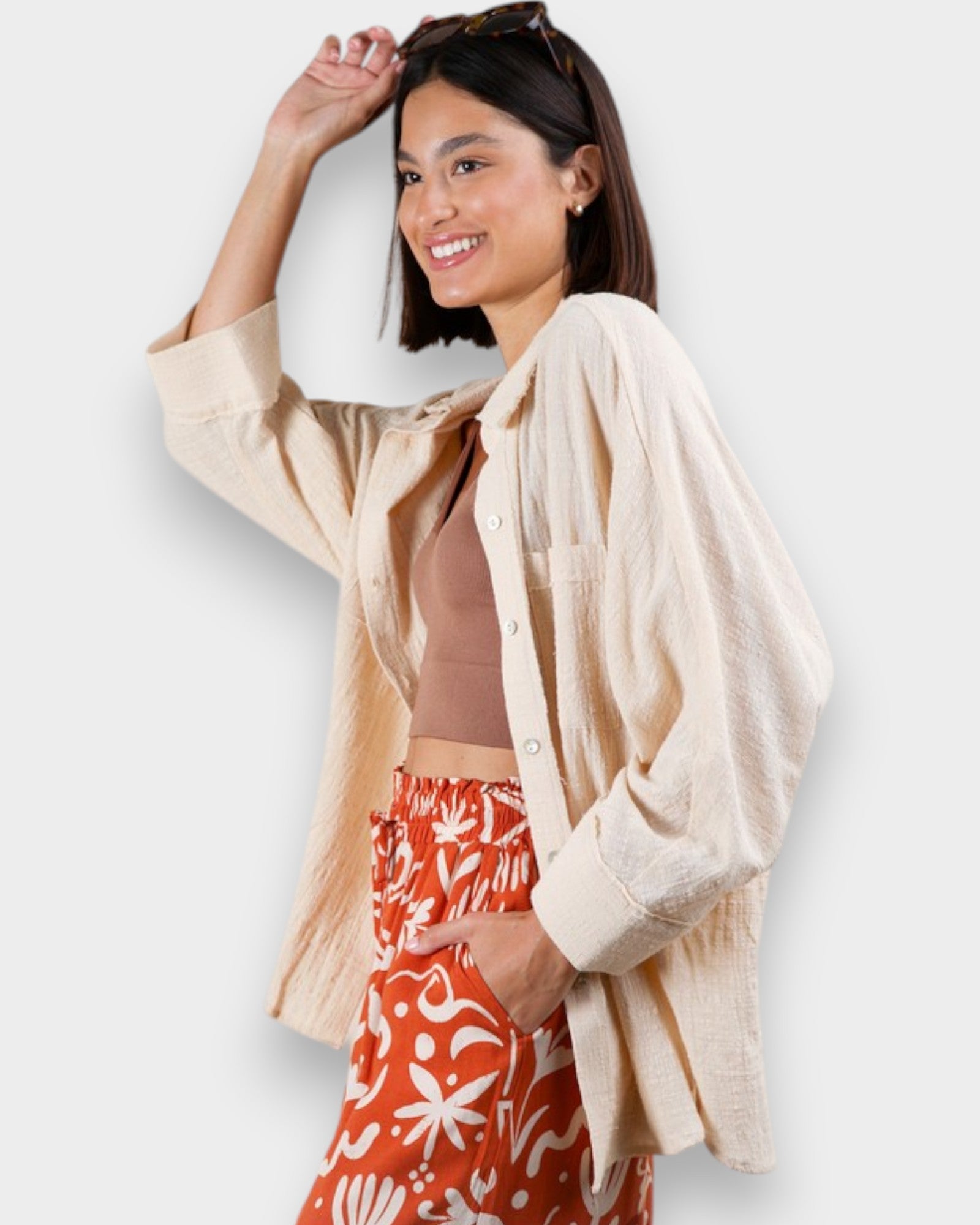 Woman wearing a beige shirt over a brown top and red patterned pants on a white background
