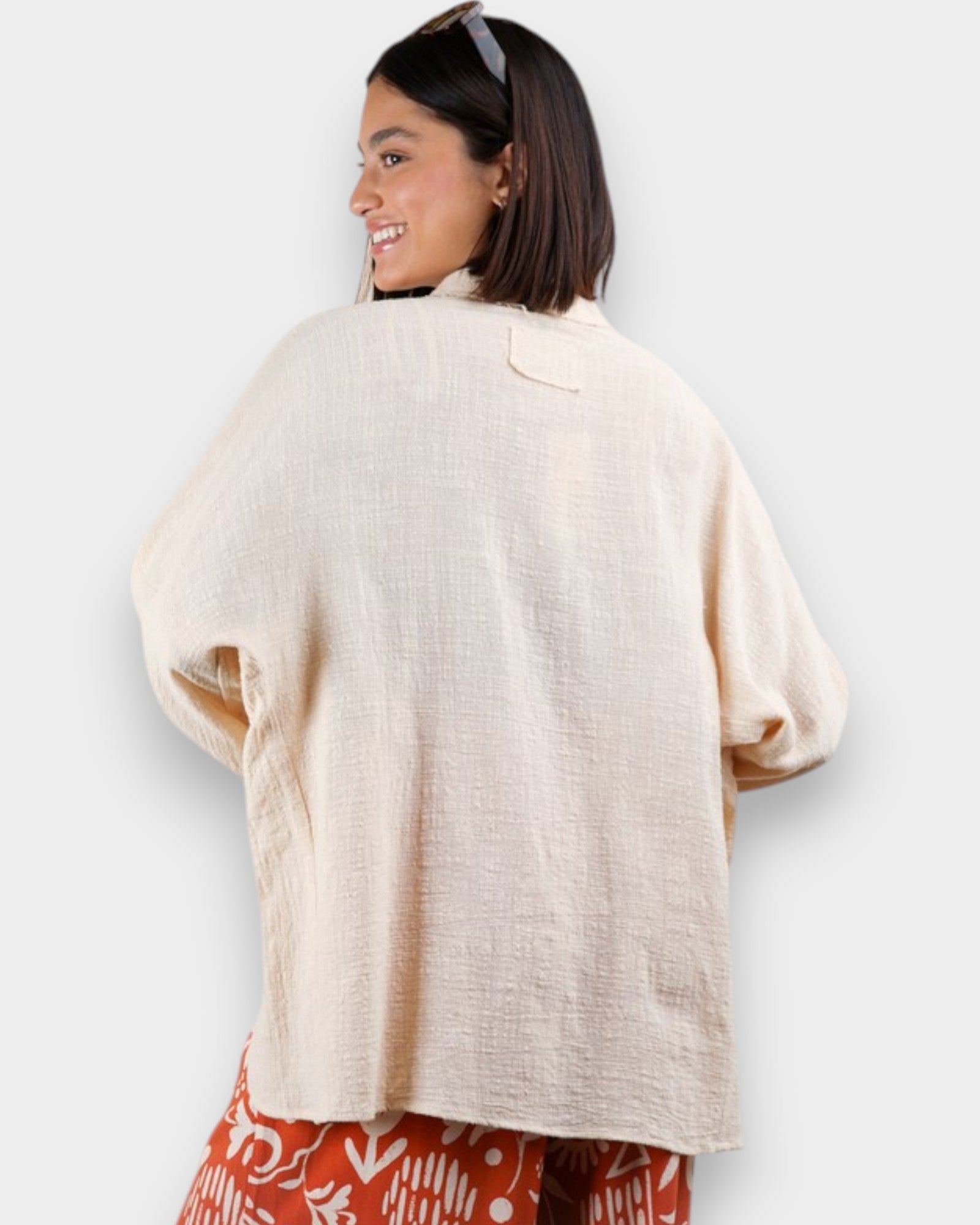 Woman wearing a beige cardigan over a patterned outfit on a white background