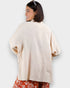 Woman wearing a beige cardigan over a patterned outfit on a white background