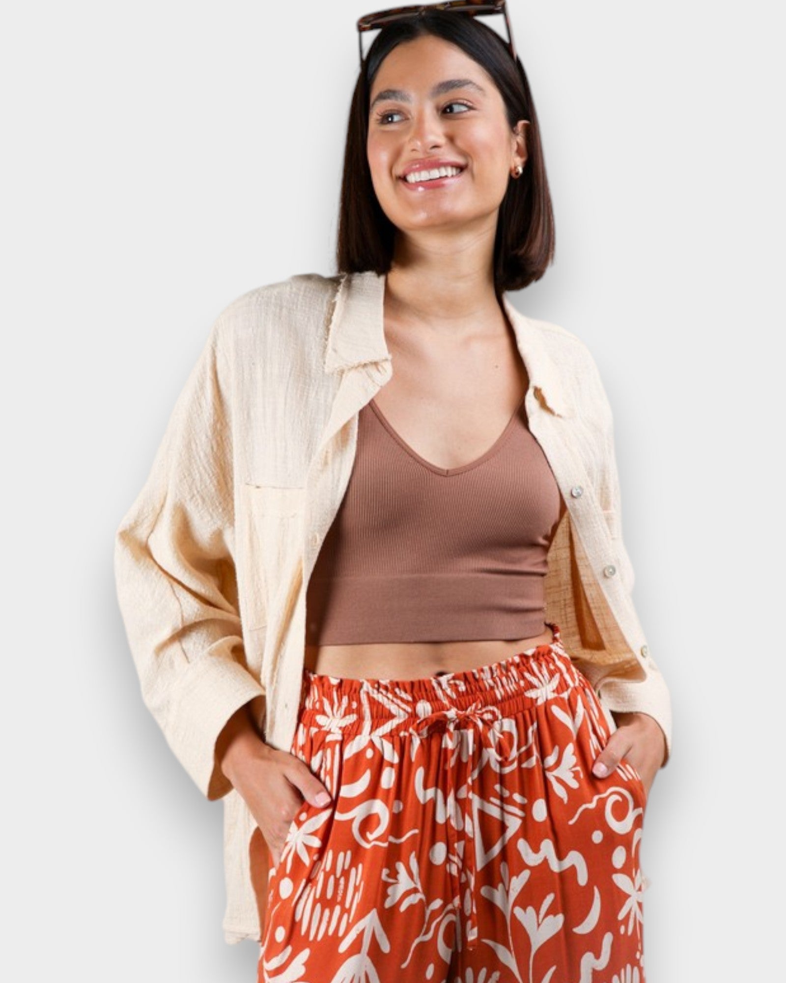 Woman wearing a beige jacket, brown top, and red patterned pants against a white background