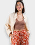 Woman wearing a beige jacket, brown top, and red patterned pants against a white background