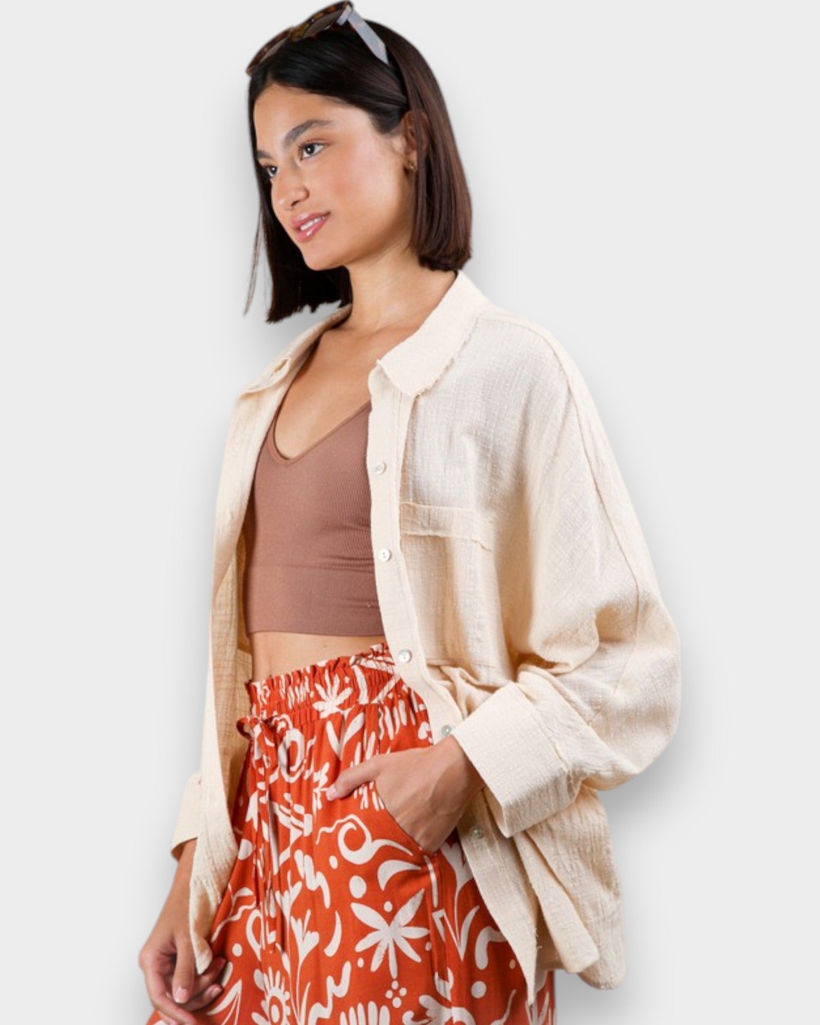 Woman wearing a beige shirt over a brown top and red patterned skirt on a white background