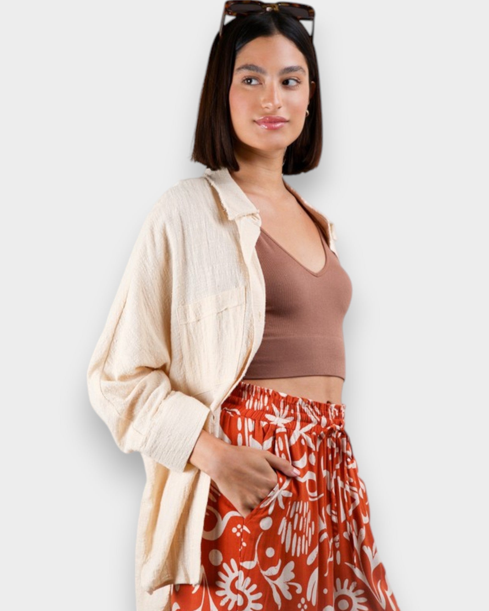 Woman wearing a beige cardigan, brown top, and red floral skirt against a white background