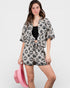 Woman wearing a black and white patterned kimono-style outfit with a pink bag on a light gray background