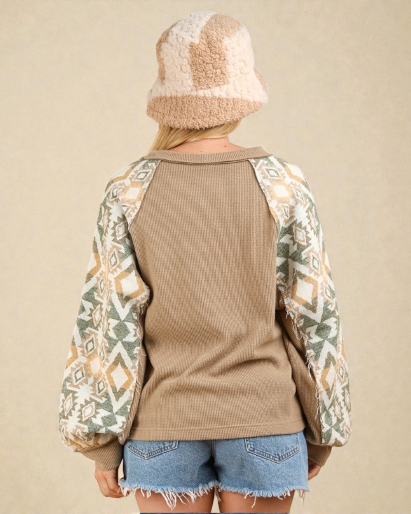 Person wearing a brown sweater with patterned sleeves and denim shorts on a beige background