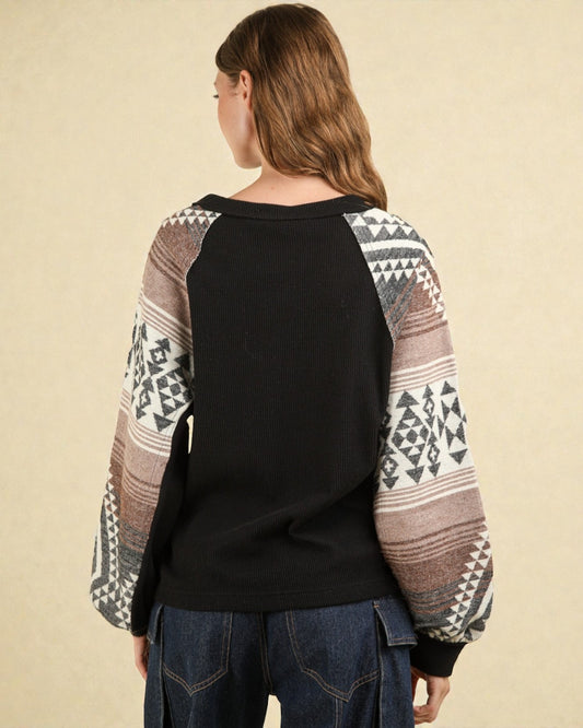 Person wearing a black sweater with patterned sleeves on a beige background