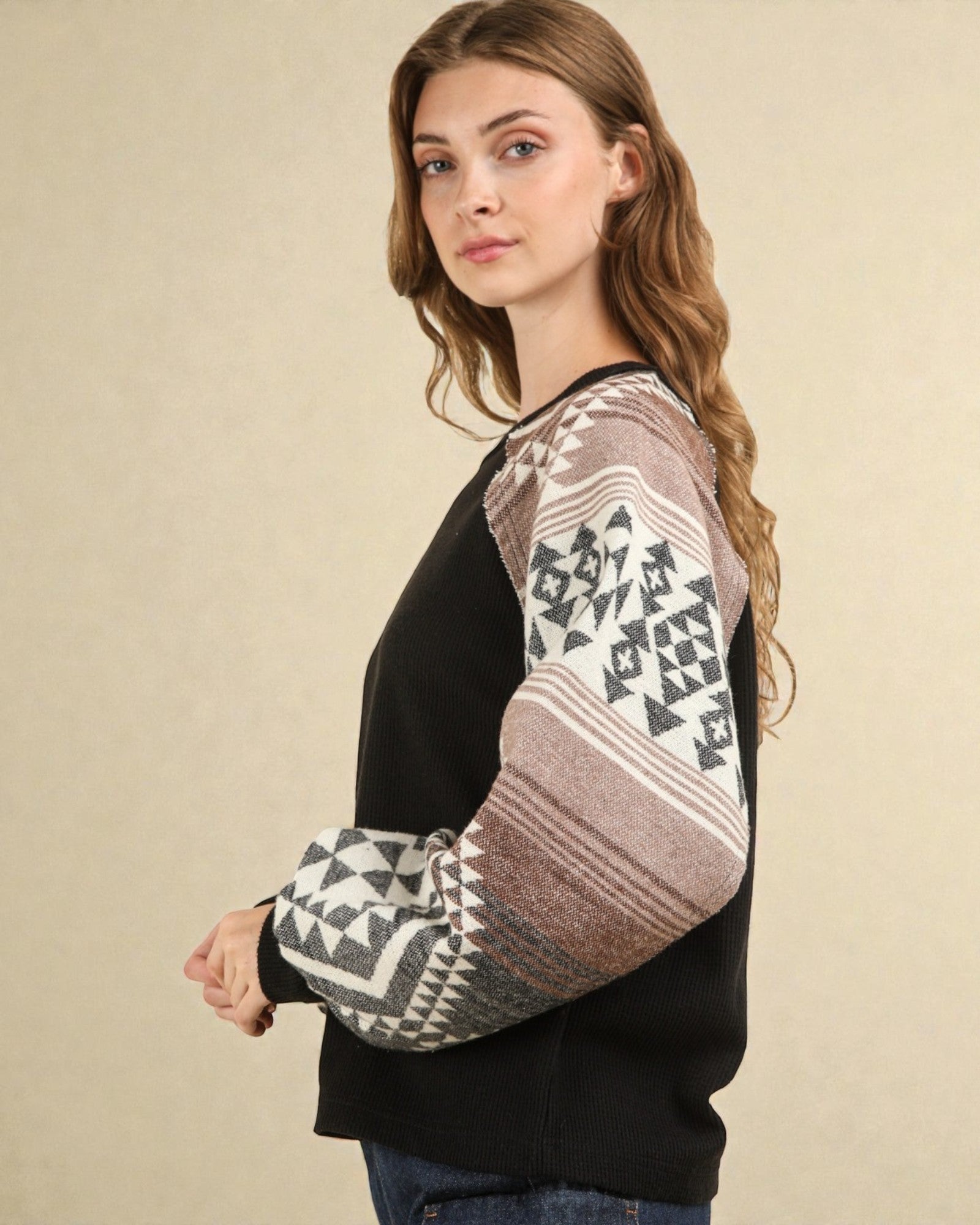 Woman wearing a black sweater with patterned sleeves against a beige background