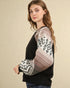 Woman wearing a black sweater with patterned sleeves against a beige background