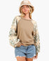 A woman wearing a tan crewneck sweatshirt with patterned raglan sleeves, paired with denim shorts and a knit bucket hat, against a plain white background.
