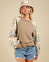 Woman wearing a brown sweater with patterned sleeves and denim shorts on a beige background
