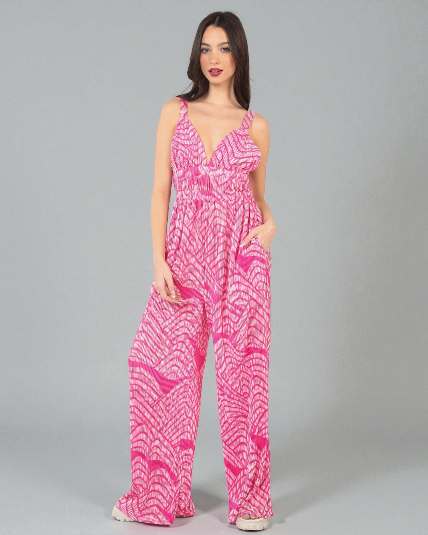 Woman wearing a pink patterned jumpsuit on a gray background