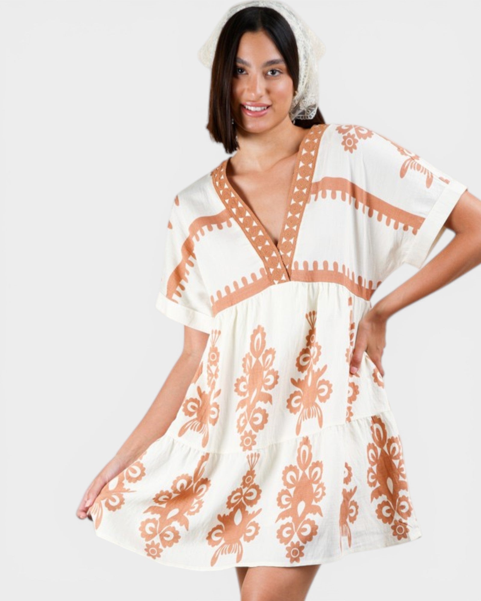 Woman wearing a white dress with orange patterns on a plain background