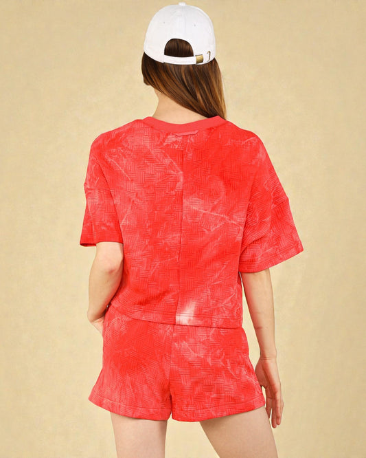 Person wearing a red tie-dye outfit with a white cap on a beige background