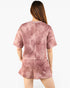 A woman viewed from the back wearing a dusty rose pink patterned short-sleeve crop top and matching shorts against a plain white background.
