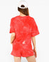 A woman viewed from behind wearing a matching red tie-dye short-sleeve top and shorts set, paired with a white baseball cap, against a plain white background.
