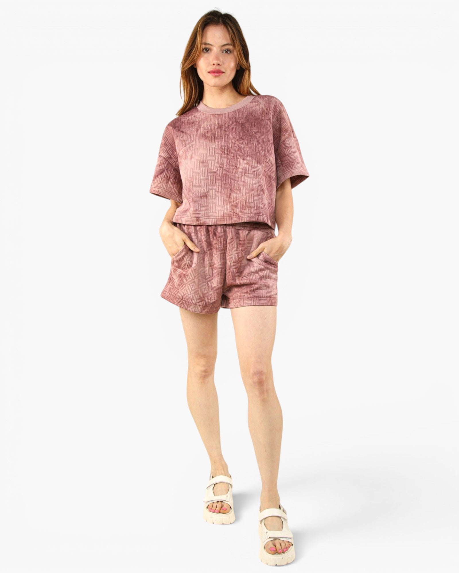 A woman modeling a matching two-piece lounge set consisting of a short-sleeve t-shirt and shorts in a dusty rose pink color with a subtle marbled texture, paired with white platform sandals, against a plain white studio background.