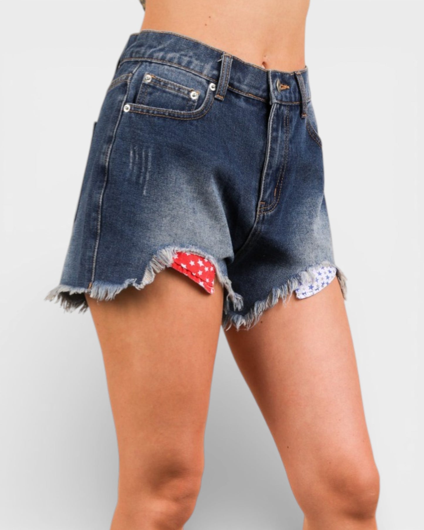 Denim shorts with a red and white polka dot patch on a plain background