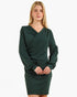 A blonde model wearing a dark forest green long-sleeve wrap-style mini dress against a plain white background.