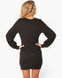 A woman shown from the back wearing a black long-sleeve mini dress, standing with hands on hips against a plain white studio background.