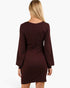 A woman viewed from the back wearing a long-sleeve, bodycon mini dress in a deep burgundy or maroon color, set against a plain white studio background.