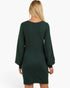 A woman viewed from the back wearing a dark forest green long-sleeve dress with a crew neck and a straight, knee-length silhouette, set against a plain white studio background.