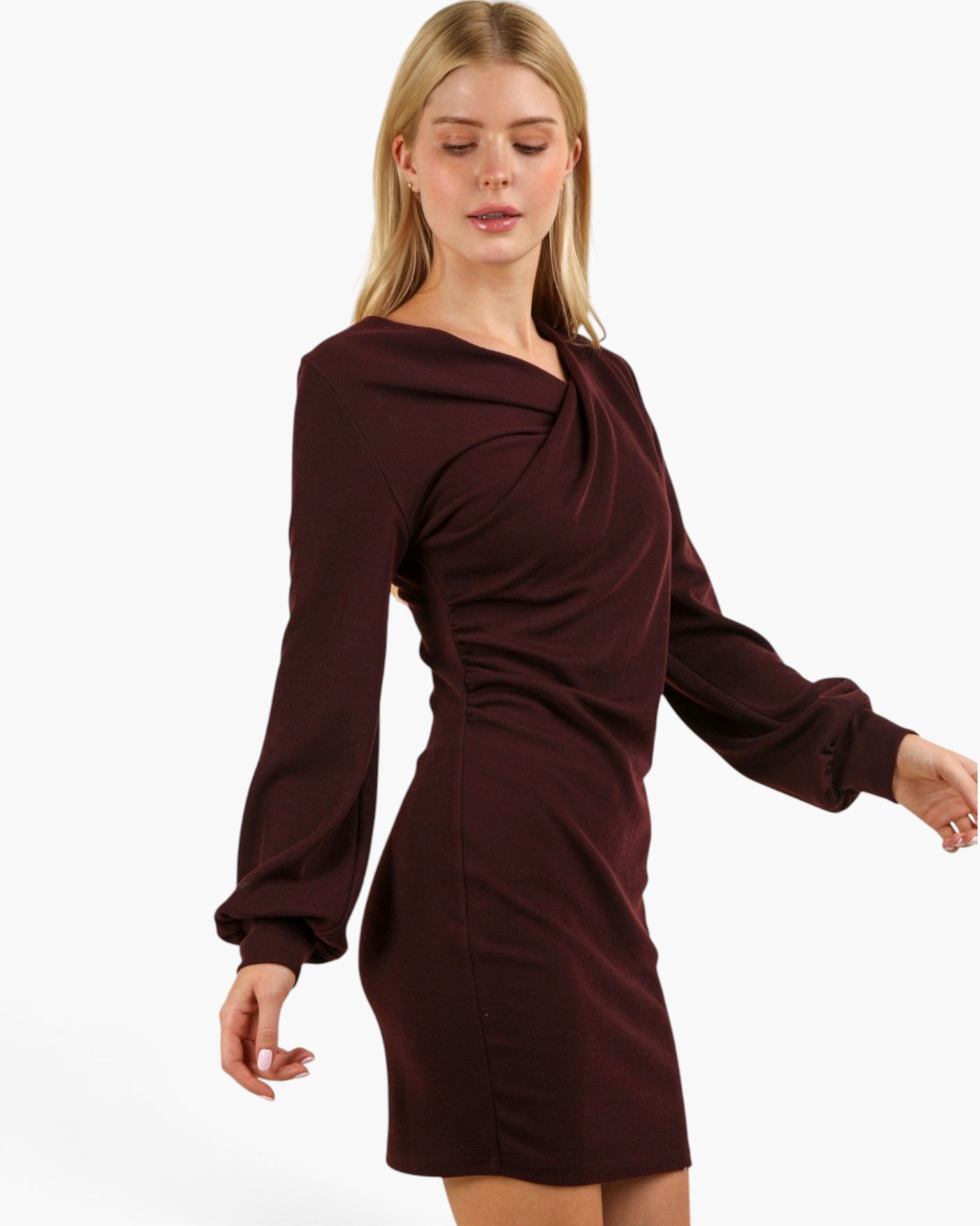 A woman wearing a long-sleeve, dark burgundy mini dress with a draped, asymmetrical neckline, shown against a plain white studio background.