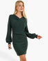 A woman modeling a dark green long-sleeve bodycon mini dress with a crossover wrap-style neckline, photographed against a plain light gray studio background.