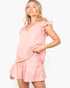 A woman modeling a light pink crinkled two-piece set consisting of a ruffled short-sleeve top and matching ruffled shorts against a plain white background.