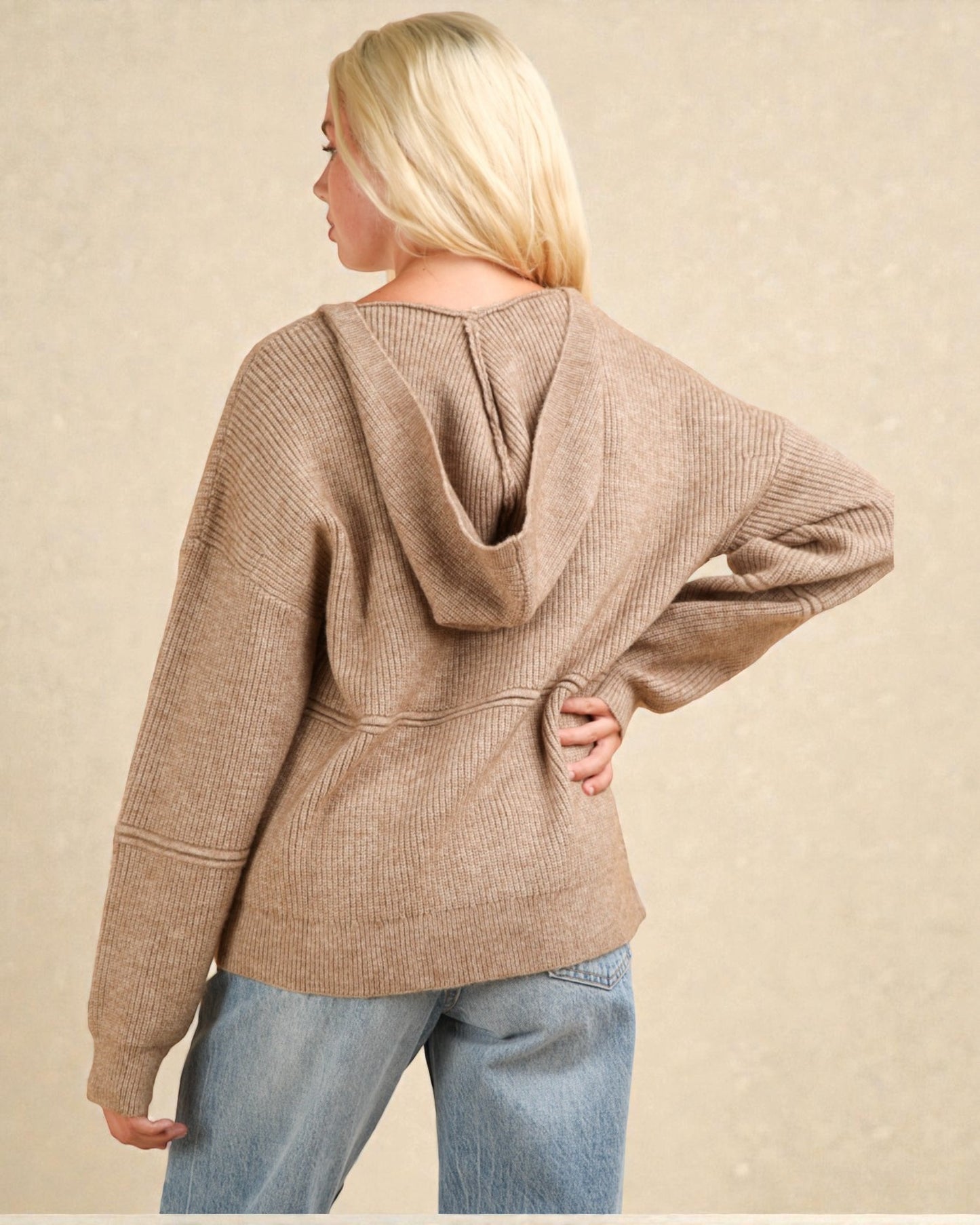 Person wearing a brown hoodie and blue jeans against a beige background