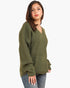 A woman wearing an olive green ribbed knit sweater with a V-neck and long sleeves, paired with blue jeans, photographed against a plain white background.