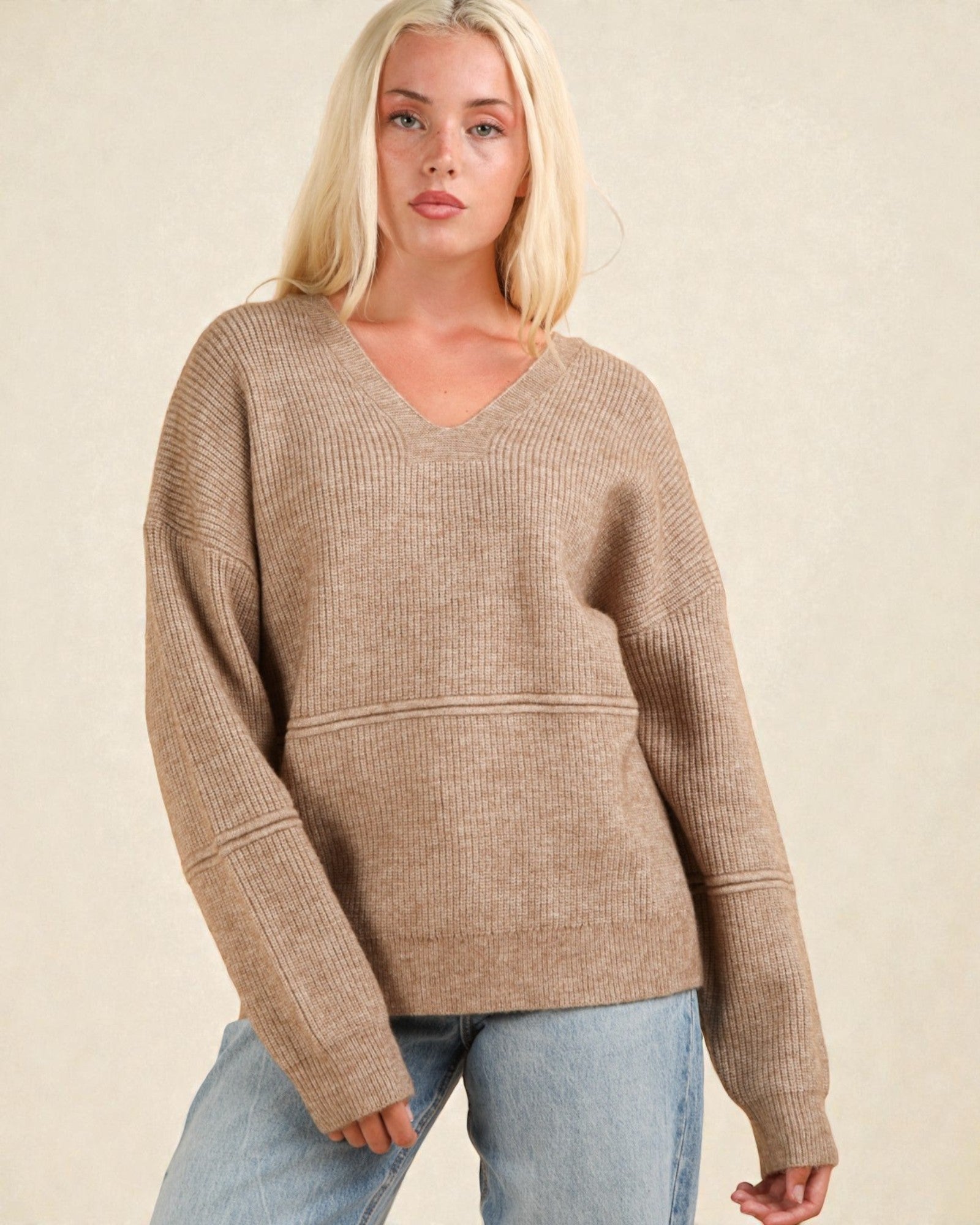Woman wearing a beige sweater and light blue jeans against a beige background