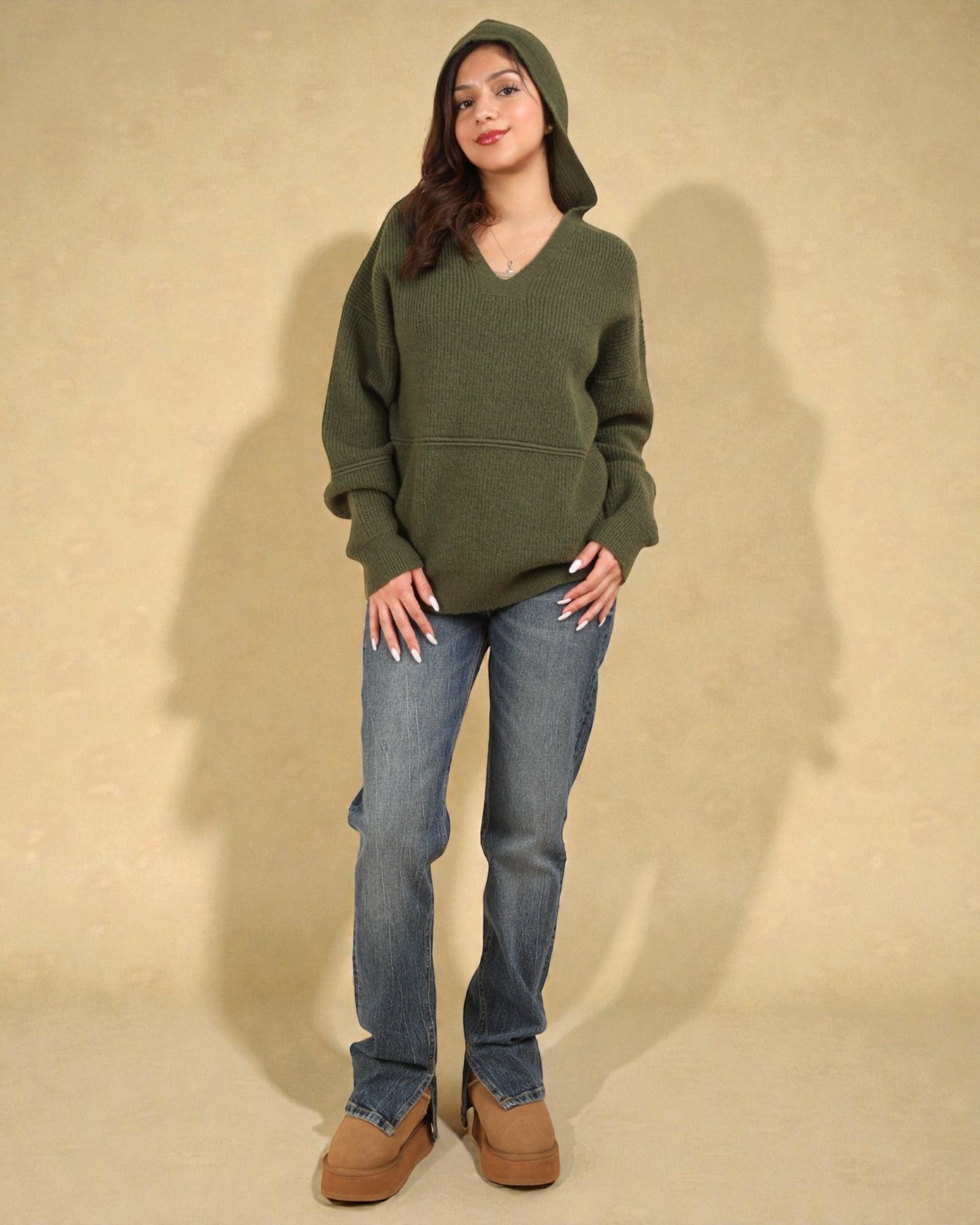 Person wearing a green hoodie and blue jeans against a beige background