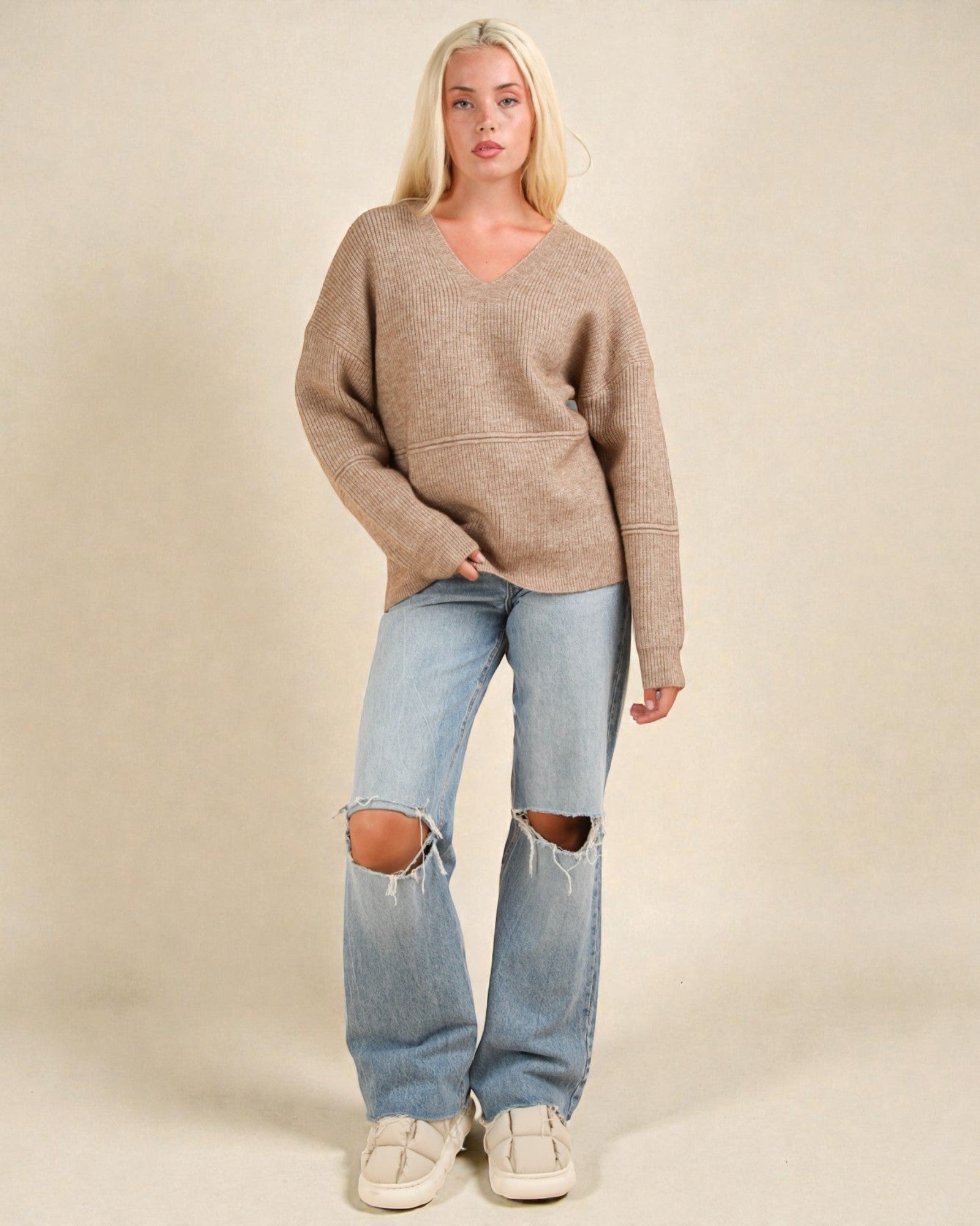 Woman wearing a brown sweater and ripped jeans on a beige background
