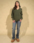 Person wearing a green hoodie and blue jeans against a beige background