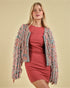 Woman wearing a colorful knit cardigan over a red dress on a beige background