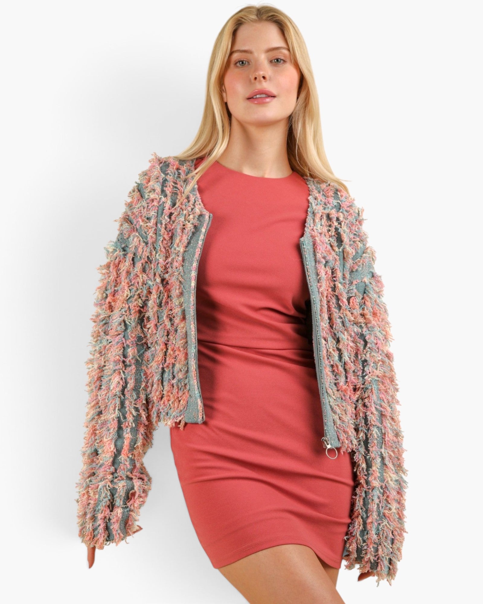 A woman modeling a textured, fringed open-front jacket in a dusty pink, blue, and gray colorway over a solid coral pink dress, set against a plain white studio background.