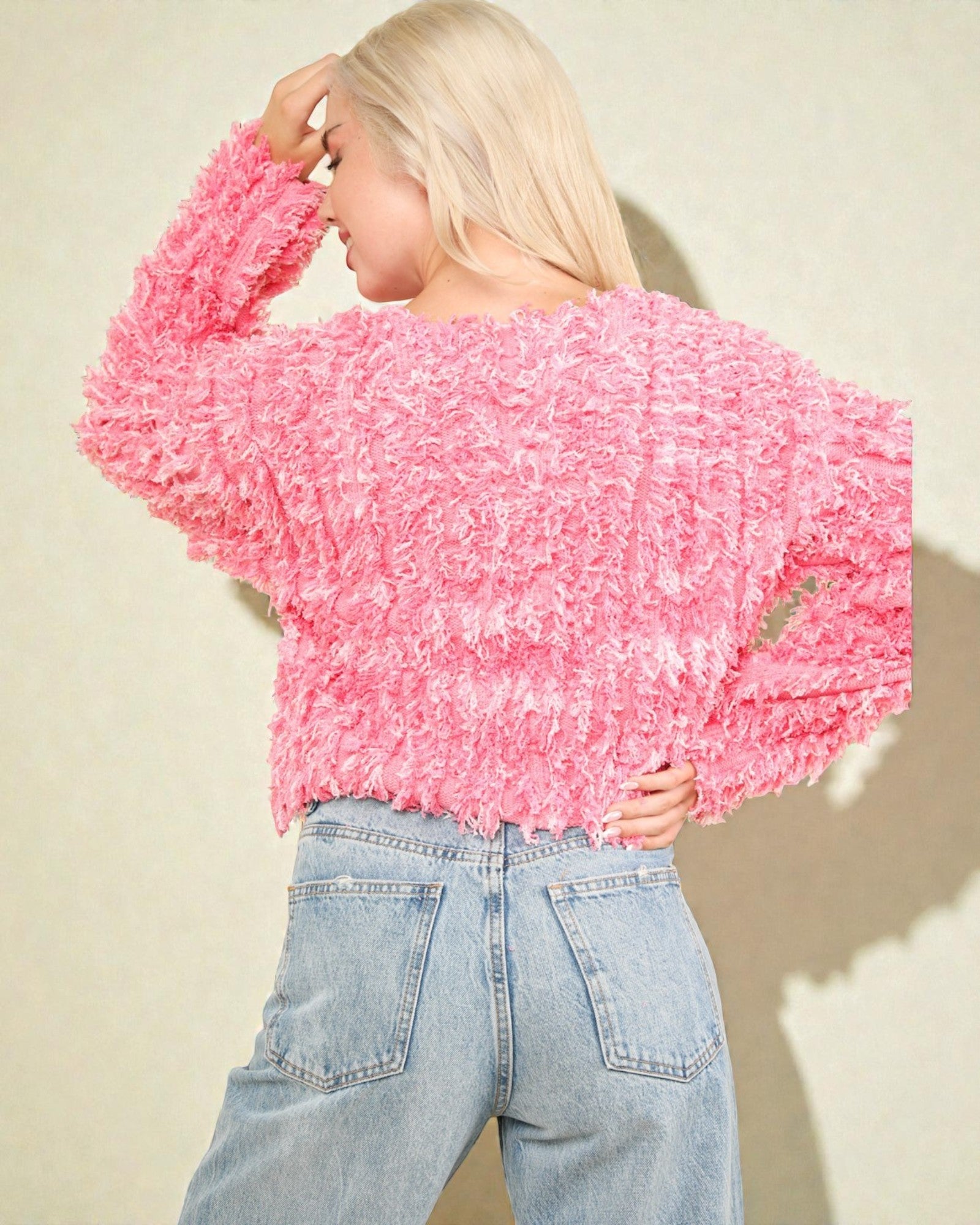 Person wearing a pink textured sweater and light blue jeans against a beige background