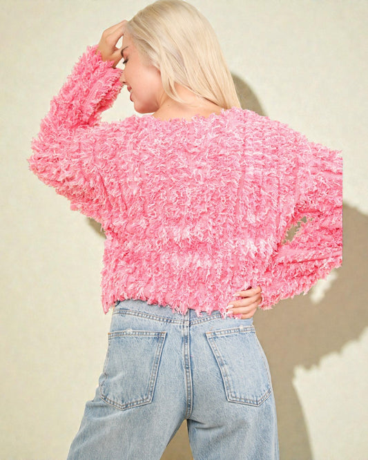 Person wearing a pink textured sweater and light blue jeans against a beige background