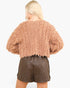 A model shown from the back wearing a textured, fuzzy cropped sweater in a dusty rose color and dark brown quilted faux-leather shorts against a plain white background.